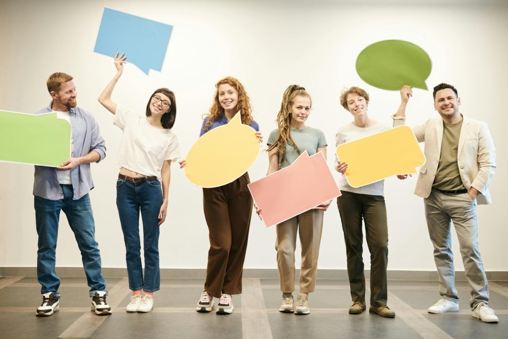 pexels photo 3184399 3184399 Diverse group of smiling adults holding vibrant speech bubbles indoors.