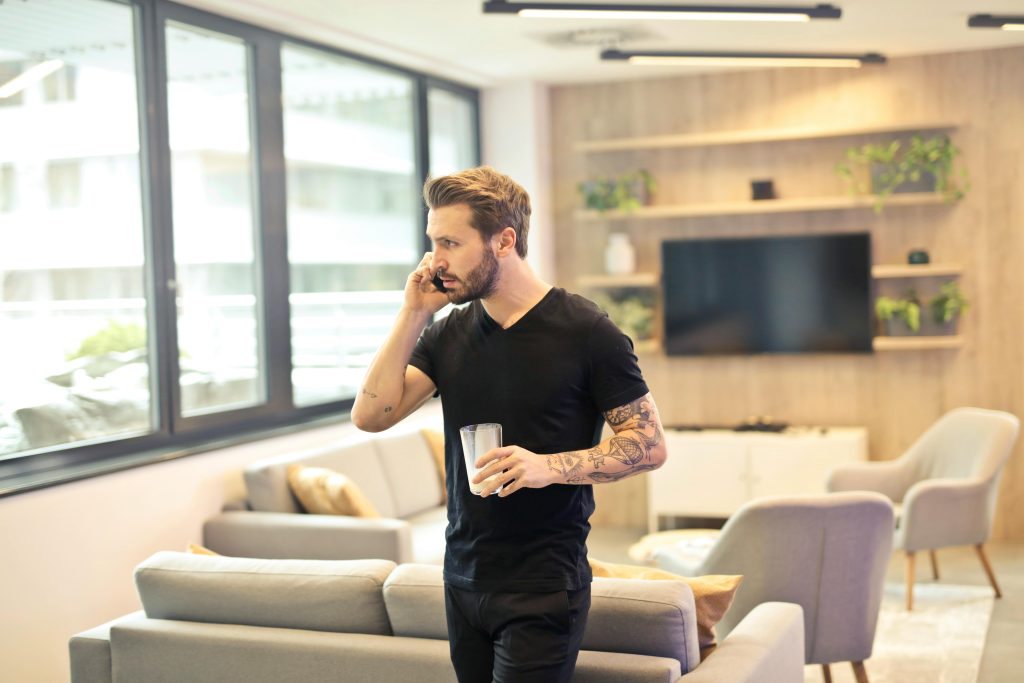 pexels photo 941710 941710 A tattooed man talking on a smartphone and holding a drink in a contemporary living room setting.